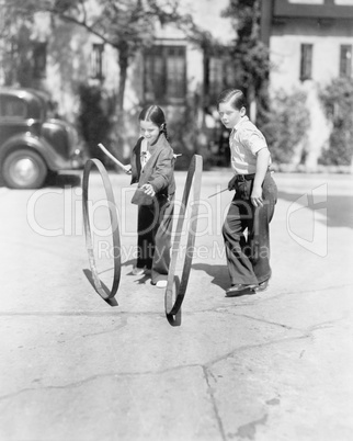 Boy and girl playing hoop and stick on a sidewalk