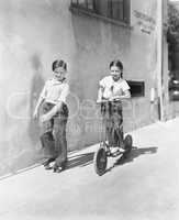Boy and girl playing on a scooter and the other on roller blades