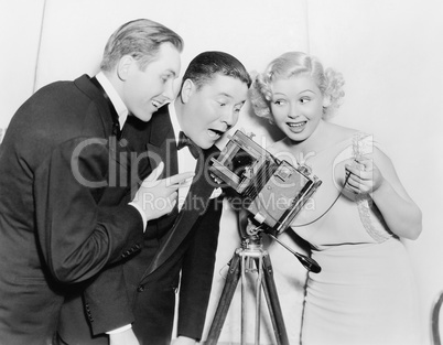 Three people looking through a camera and laughing