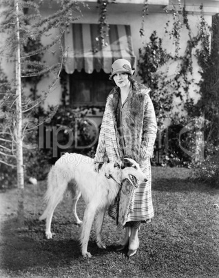 Young woman in coat and hat standing outside with her Russian Wolfhound