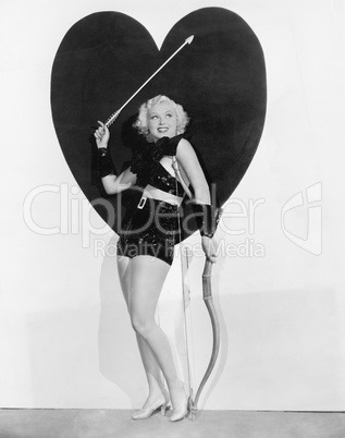 Young woman dressed up as cupid standing in front of a big heart