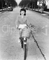 Young woman riding her bicycle with basket full of flowers and carrots