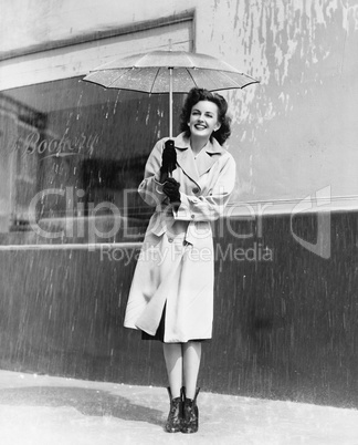 Young woman in a raincoat and umbrella standing in the rain