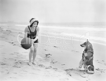 Young woman playing with her dog and ball on the beach