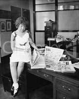 Girl sitting on a desk and reading a newspaper
