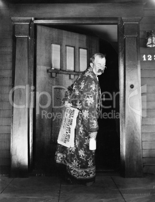 Man walking into the house with newspaper and milk in hand