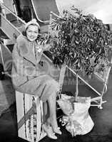 Woman sitting on a crate of oranges next to a plane and citrus tree