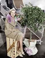 Woman sitting on a crate of oranges next to a plane and citrus tree