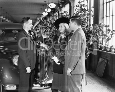 Man and woman standing in a car showroom talking to a salesman