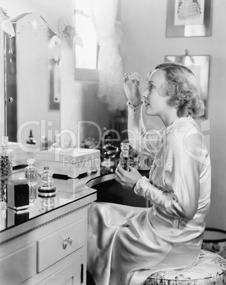 Woman sitting in front of her vanity putting perfume on her eyebrows