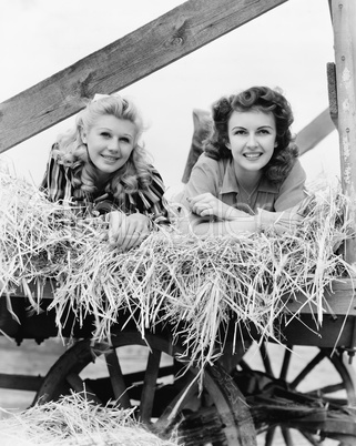 Two women lying in a wagon of hay with their legs in the air