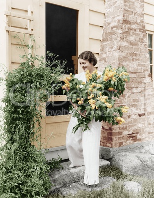 Woman in front of her house gathering flowers in her arms