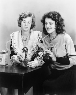 Two woman sitting together at a table repairing their shoes
