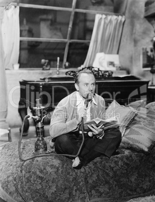 Man sitting on a bed smoking his water pipe