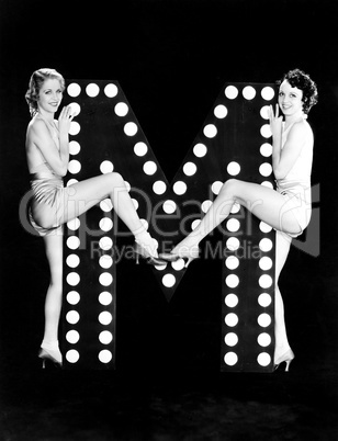 Two young women posing with the letter M