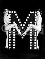 Two young women posing with the letter M