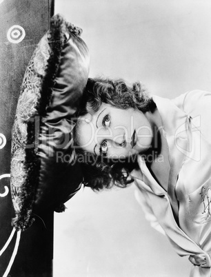 Portrait of a young woman pressing her head against a cushion on the wall