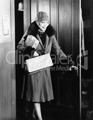 Young woman in a coat and hat entering into a room