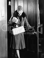 Young woman in a coat and hat entering into a room