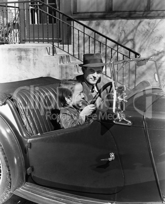 Young boy sitting in the driver's seat of car with his father