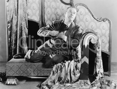 Portrait of a man sitting on a couch holding a fan