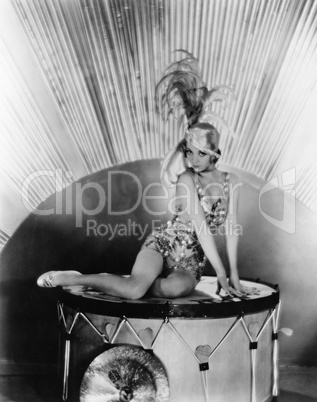 Portrait of a young woman sitting on a drum with a feather hat