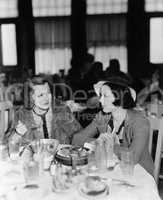 Two young women sitting in a restaurant and looking at each other