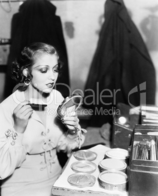 Young woman with a make up brush looking at her face in a hand mirror