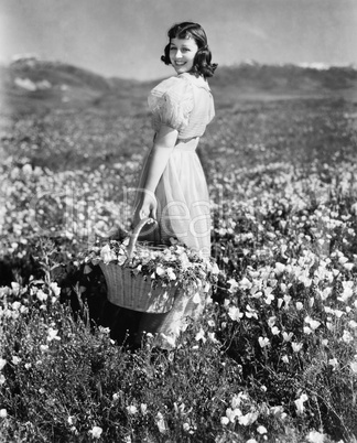 Rear view of a girl standing in a meadow holding a flower basket and smiling