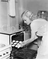 Young woman taking cookies out of an oven