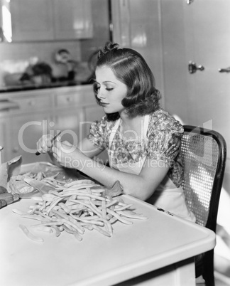 Young woman sitting on a chair and cutting beans