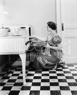 Profile of a young woman putting a pie into an oven