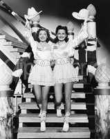 Two young women stepping down a staircase waving their western hats