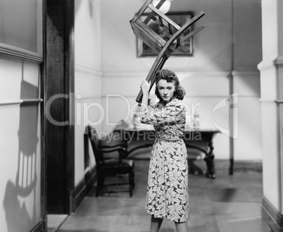 Young woman holding a chair above her head in anger