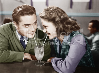 Couple in a restaurant looking at each other and sharing a milk shake with two straws