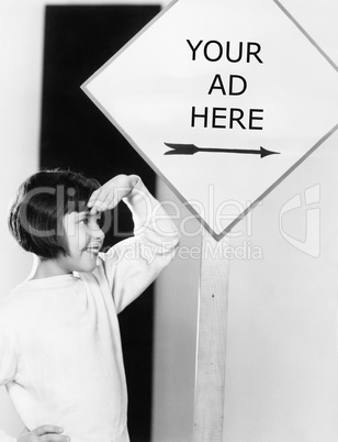 Profile of a young girl shielding her eyes under an information board