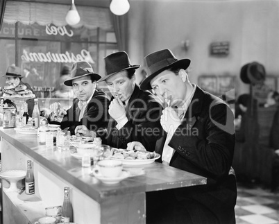Three men with hats eating at the counter of a diner