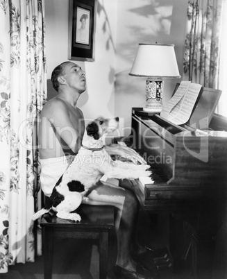 Man playing a piano with his dog next to him