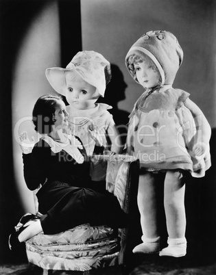 Woman sitting on a chair and looking at two oversized dolls