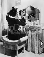 Woman putting on a hat in front of a dressing table