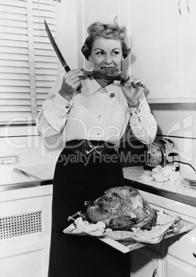 Woman eating roast turkey in her kitchen with a knife in her hand