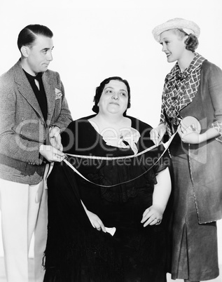Male tailor and his assistant measuring an overweight woman with a measuring tape