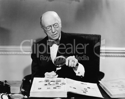 Senior man examining a postage stamp with a magnifying glass