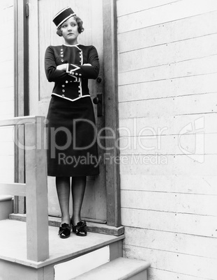 Young woman in a uniform standing with her arms crossed in front of a closed door