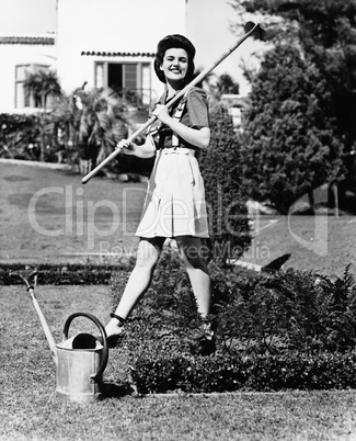 Profile of a young woman carrying a rake on her shoulder in a garden