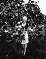 Portrait of a young woman holding grapefruits and standing in an orchard