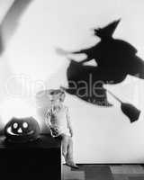 Boy sitting on a table with a pumpkin and a shadow of a witch on a wall