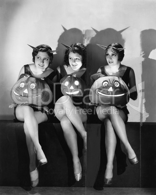 Three young women sitting and holding Jack O' Lanterns on their laps