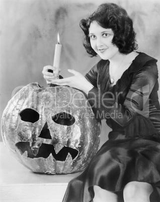 Young woman holding a burning candle on a Jack O' Lantern and smiling