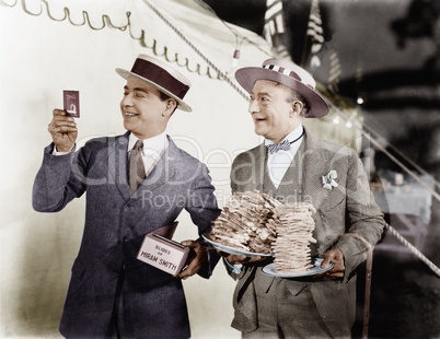 Man holding plates of sandwiches with a man looking at a film slide beside him